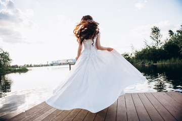 Redhead bride in a beautiful wedding dress on a wooden bridge on a lake