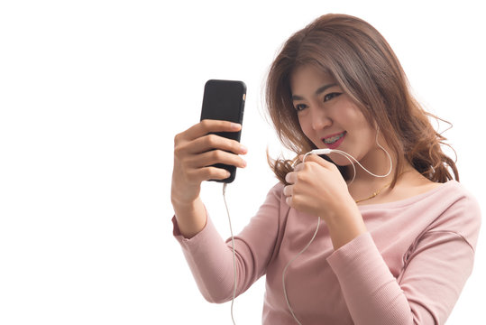 Young happy asian woman listening music with headphones from her smart phone isolated on white background. Female listening to music on headphones standing in studio. Free from copy space.