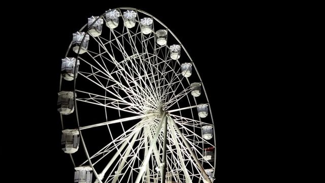 Illuminated white color colour ferris wheel spinning clockwise against black plain background at an unspecified amusement park at night