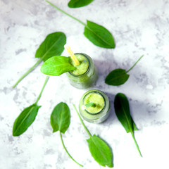 Fototapeta na wymiar Still life of green smoothie in pair of glass bottles on white textured background. Healthy lifestyle concept.