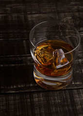 Glass of whiskey with ice cubes on wooden table