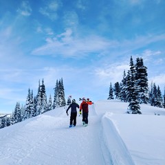 Two skiers hiking up a slope on a blue sky day