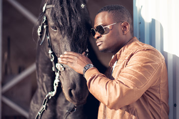 african Man wearing sunglasses near a black horse in hangar