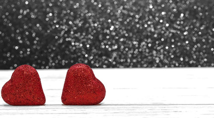 Two shiny red hearts on a wooden table with a blurred colorful background