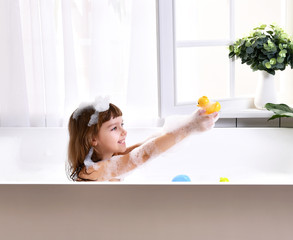 Obraz na płótnie Canvas Happy little baby girl sitting in bath tub in the bathroom