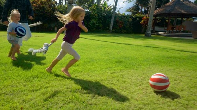 Father plays football with two little daughters on green grass lawn in front of ocean