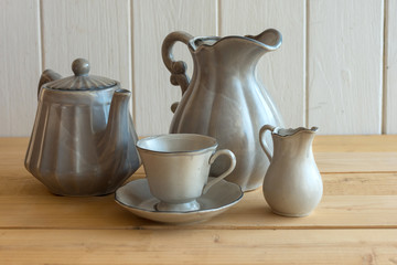 Tea set is Gray on a wooden background. Teapot, creamer, Cup and saucer on the table. Ceramic kitchenware