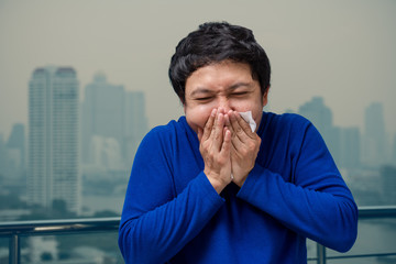 Fototapeta na wymiar Asian man wearing the face mask against air pollution with coughing at the balcony of High Apartment which can see pollution and heavy fog over the bangkok cityscape background, healthcare concept