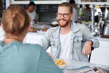 Stylish two men have conversation while sit at cozy coffee shop, discuss new project ideas, have rest in free time. Attrctive journalists speak about details of teamwork. Friends talk during meeting