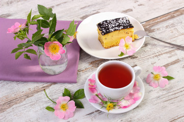 Cup of tea with cheesecake and wild rose flower on rustic board