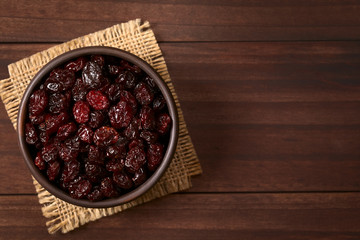 Dried cranberries in small rustic bowl, photographed overhead on dark wood with natural light (Selective Focus, Focus on the cranberries on the top)