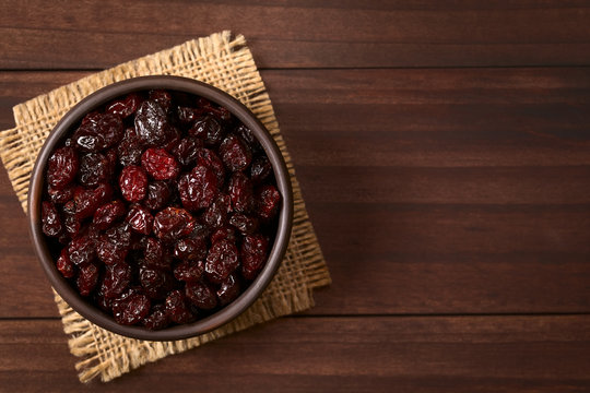 Dried cranberries in small rustic bowl, photographed overhead on dark wood with natural light (Selective Focus, Focus on the cranberries on the top)