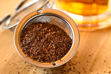 Rooibos herbal tea in strainer with freshly prepared tea in the back, photographed with natural light (Selective Focus, Focus one third into the leaves)
