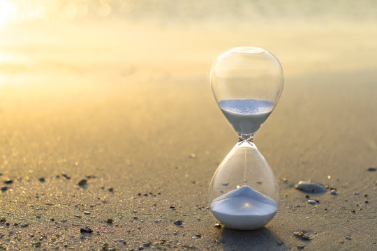Hourglass close up in a warm golden morning sunlight on a sandy beach starting time for a new day or running of time with side copy space.