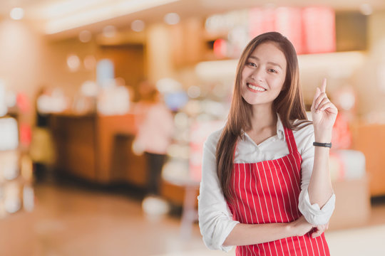 Portrait of Smiling beautiful young Asian woman wear red apron and hand pointing with copy space for your text or advertising isolated on white.