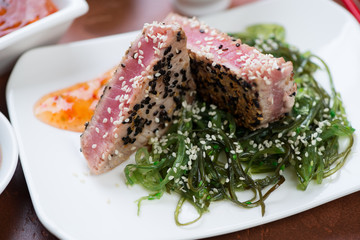 Close-up of tuna steak fried with sesame seeds and served on a bed of seaweed salad, selective focus