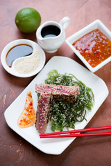 Roasted tuna steak served with chuka salad and dipping sauces, vertical shot on a rusty metal background, selective focus