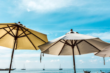 Obraz na płótnie Canvas Canvas beach umbrellas against light blue sky with soft clouds. Tourist boats floating near the beach in the background.