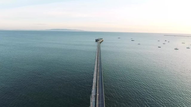 Aerial Flyover - Coastal sunset drone view with a pier pointing out to sea.