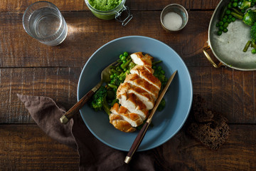 Bowl with сhicken steak, fried vegetables on dark wooden table