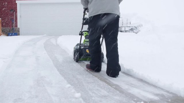A man snowblowing his driveway during a blizzard
