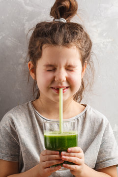 Beautiful happy little girl drinking healthy green vegetable-fruit juice. Healthy children vegan food concept.