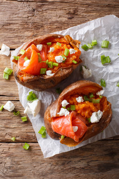 Healthy food: sweet potato stuffed with salmon, feta cheese and green onions close-up on parchment. Vertical top view