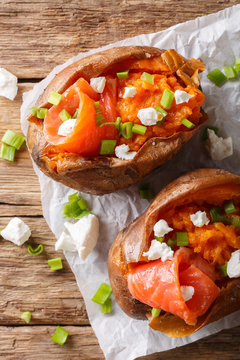 Organic food: baked sweet potato stuffed with red fish and green onion close-up on paper. Vertical top view