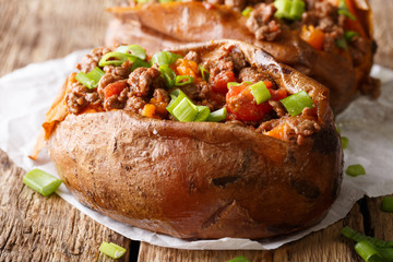 Baked sweet potatoes stuffed with ground beef with tomatoes and onions macro on paper. horizontal