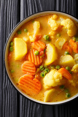 Vegetable curry of potatoes, carrots, cauliflowers, peas, tomatoes close-up in a bowl. Vertical top view