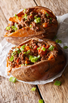Healthy food: sweet potato stuffed with ground beef with tomatoes and onions close-up on paper on the table. vertical