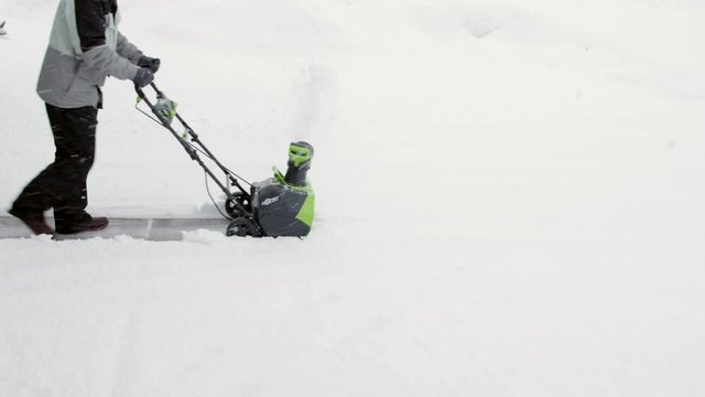 A man snowblows his driveway in a blizzard