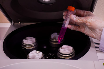 Centrifuge machine with a hand holding a purple cell sample