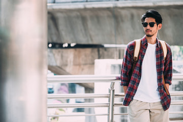 Portrait of young asian man in casual clothes with sunglasses and backpack on urban scene...