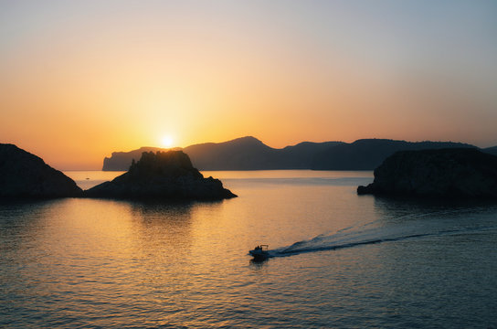 Fototapeta The boat yacht sails near Santa Ponsa coastline at sunset in Morro d'en Pere Joan bay in Mallorca, Balearic islands of Spain. Es Malgrat rocks.