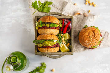 Vegan beet chickpea burgers with vegetables, guacamole and rye buns in wooden box. Healthy vegan...