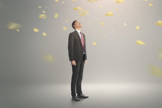 Young asian businessman looking up with falling confetti