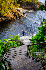 A woman looking through binoculars on a flight of stairs leading to the suspension bridge in Storms River Mouth national park in South Africa