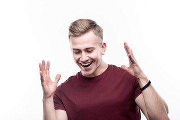 In great mood. Cheerful young man in a burgundy t-shirt making dancing moves and smiling brightly while standing against a white background