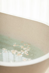 Bright Bathroom at Home. Bath with Flower Petals and Salt. Tray over the Bath with Orange Juice, Notepad and Candles.