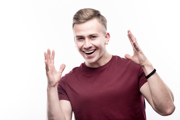 In happy mood. Handsome fair-haired young man in a burgundy t-shirt making dancing moves and smiling at the camera while posing isolated on a white background