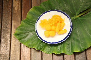 ancient Thai Dessert, thai sweet dessert in plate on green leaf and wooden table background with copy space for text, egg yoke fudge balls cooked in syrup, Pinched gold egg yolks, appetizer