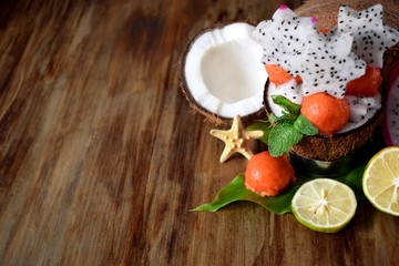 Tropical fruits. Papaya balls, coconuts, limes and pitahaya carved stars on a wooden table