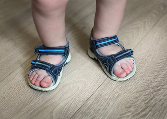 Shod legs of the baby. Children's sandals on their feet. Toddler shoes. Tourist sandals for the smallest travelers. A new purchase in a shoe store.