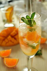 Sparkling cocktail with mango pieces, ice cubes and mint in a wineglass