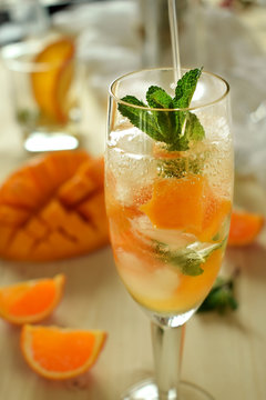 Sparkling cocktail with mango pieces, ice cubes and mint in a wineglass