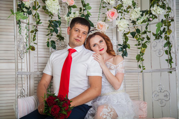 the bride and groom in a light interior against a floral arch background. Wedding in red shades