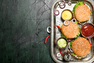 Burgers from fresh beef and vegetables with different sauces on a steel tray.