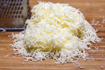 Shredded mozzarella cheese on a cutting board with a grater