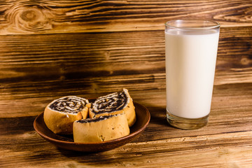 Ceramic plate with poppy seed buns and a glass of milk on wooden table